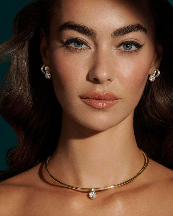 Model wearing a gold collar necklace with a diamond pendant and matching earrings from the Elizabeth Taylor Collection